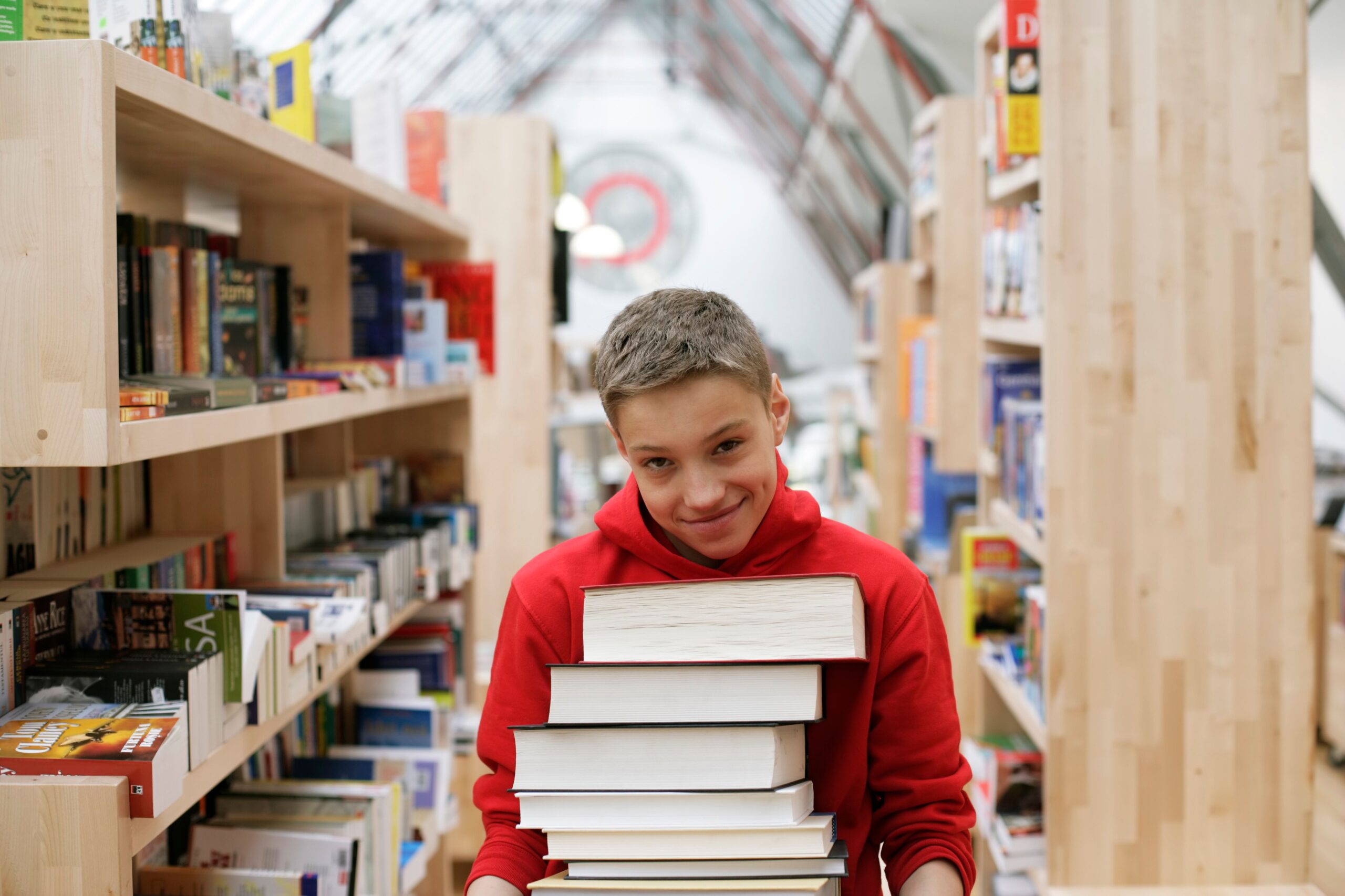 Smiling teenager holding a stack of books in a contemporary library setting.